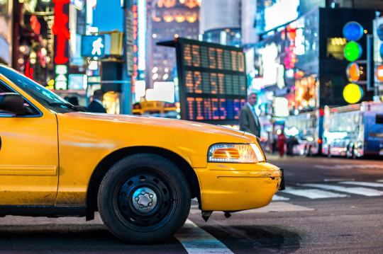 Gelbes Taxi auf den bunten Straßen von New York in der Nacht, im Hintergrund funkeln die Lichter der Stadt