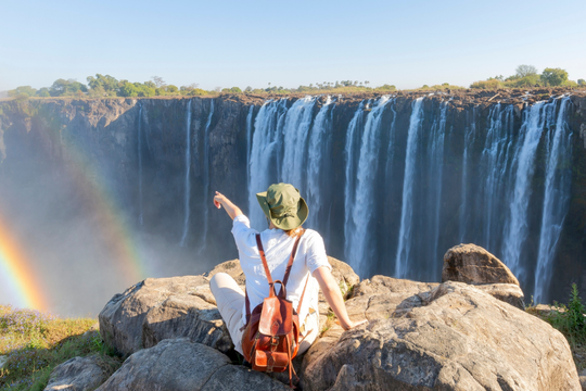 Person mit Rucksack sitzt auf Klippe und schaut zum Wasserfall